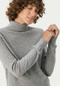 Grauer Strickpullover mit hohem Kragen, taillierten langen Ärmeln und gerippten Bündchen. Weiche Textur mit einem subtilen Schimmer.
