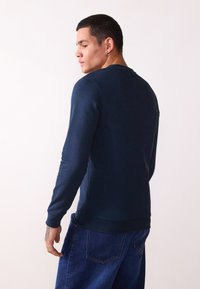 Navy blue long-sleeve sweatshirt made of smooth fabric, featuring a crew neck and ribbed cuffs, paired with denim jeans.