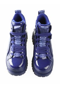 Zapatillas altas de charol púrpura con lengüeta de tela texturizada, suela de goma gruesa y una marca prominente en los cordones y el talón.