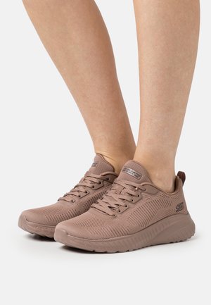 Light brown athletic shoes with a breathable mesh upper, textured design, and thick rubber sole. Features laces and brand logo on the tongue.