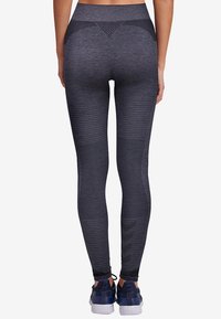 Svarta atletiska tights med hög midja, strukturerad tyg, horisontella linjemönster och en subtil logodetalj på underbenet.