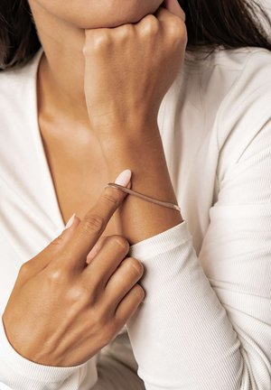 Silberarmband, das sich um das Handgelenk windet, glatte Textur, minimalistisches Design, kombiniert mit einem weißen, gerippten Langarmtop und neutralem Nagellack.