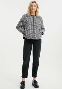 Czarna i biała kurtka z wzorem houndstooth, zapinana na zamek, z szerokimi rękawami i bocznymi kieszeniami, w połączeniu z czarnymi spodniami prostymi i butami na platformie.