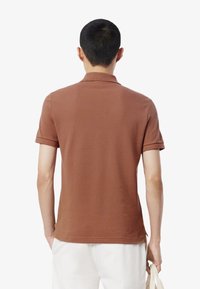 Brązowa koszulka polo z krótkim rękawem, wykonana z miękkiego materiału, z klasycznym kołnierzykiem i podwiniętymi mankietami, o gładkim, bezszwowym designie z tyłu.