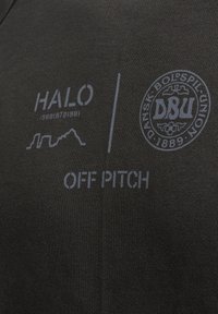 Schwarzer Stoff mit Text, der "HALO", "OFF PITCH" und ein Logo für "DBU" zeigt, alles in einer subtil kontrastierenden Farbe. Schlichtes, elegantes Design.