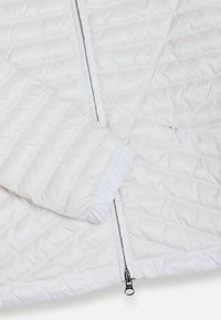 Biały pikowany rękaw kurtki i przód z widocznym srebrnym zamkiem błyskawicznym oraz elastycznym mankietem, przedstawione na białym tle.