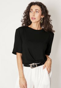 Czarny t-shirt z krótkim rękawem z gładkiego materiału o luźnym kroju i okrągłym dekolcie, połączony z białymi, zwiewnymi spodniami i dekoracyjnym czarnym paskiem.