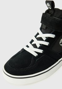 Sorte semsket mid-top sneakers med hvite lisser og detaljer, som har en teksturert stofftunge og en gummisåle med en svart stripe.