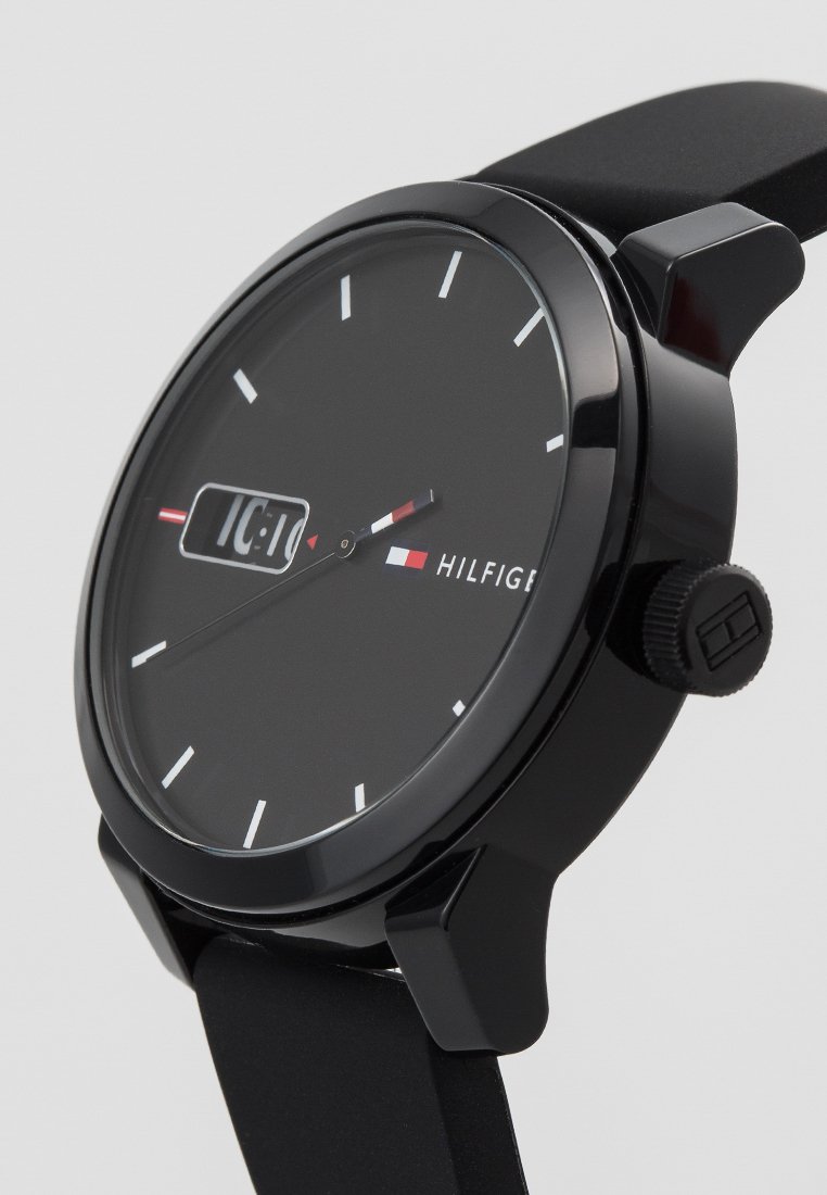 Czarny analogowy zegarek o eleganckim, minimalistycznym designie. Posiada okrągłą tarczę, białe wskaźniki godzin i teksturowany czarny silikonowy pasek.