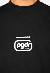 Czarna bluza z ribbrowym dekoltem. Zawiera biały logo z napisem "PEGADOR" nad stylizowanym "pgdr" z kolorowymi kropkami w niebieskim i różowym.