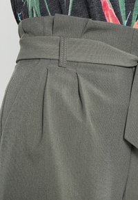 Šedé kalhoty s páskem a texturovaným povrchem, s předními záhyby a širokým pasem, doplněné vzorovaným topem.