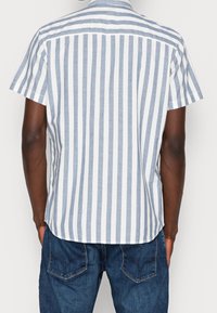 Kortärmad skjorta i ljusblå och vita ränder, med en knapp-up krage och rak nederkant, bärs med mörkblå jeans.