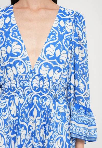 Abito blu e bianco con motivo, scollatura a V profonda, vita arricciata e maniche svasate con accenti geometrici. Tessuto leggero.