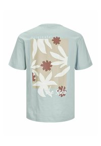 Camiseta de manga corta azul claro con estampado floral en crema y marrón, con un fondo rectangular beige y el texto "The Studio".