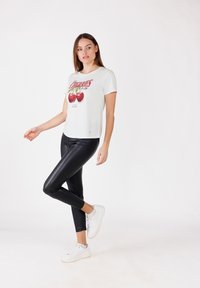 T-shirt blanc avec un graphique de cerise et du texte rouge, associé à un legging en simili cuir noir et des baskets blanches. Design simple et coupe décontractée.