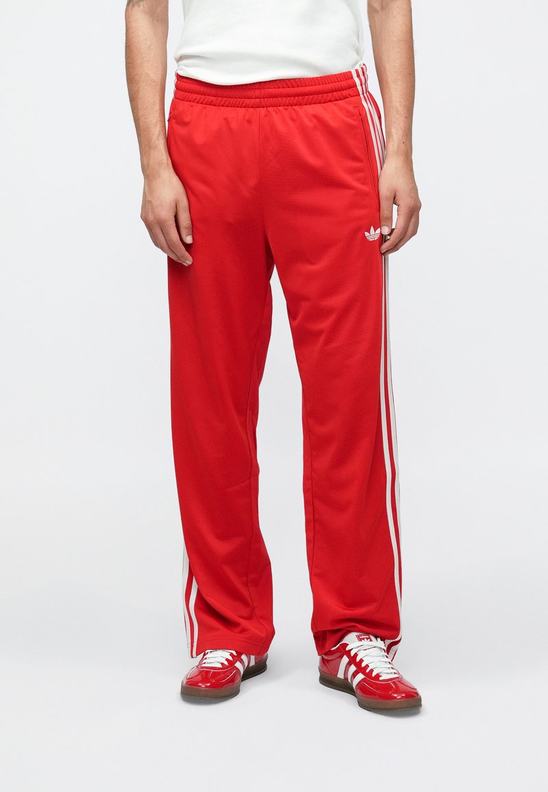 Rote sportliche Hose mit lockerem Schnitt aus glattem Stoff. Verfügt über weiße Seitenstreifen und ein gesticktes Logodetail am oberen Bein.