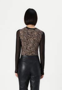 Il bodysuit a maniche lunghe presenta un retro con stampa leopardata e un davanti nero trasparente. Abbinato a pantaloni in pelle neri a vita alta.