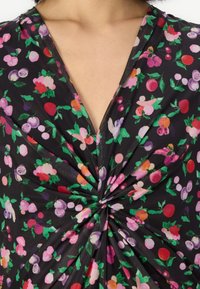 Tissu noir avec un motif floral mettant en vedette des fruits et des fleurs colorés, avec un détail de design tordu au centre.