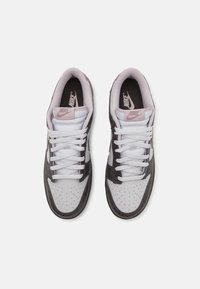 Nike sneakers met een bovenwerk van wit leer en grijze gestructureerde accenten, geperforeerde neuzen en witte veters. Roze merknaam op de tong.