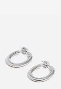 Srebrne kolczyki-koła o zaokrąglonym, litery U kształcie. Wykonane z metalu, z gładkimi powierzchniami i zapięciem na zatrzask.