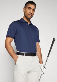 Tengerészhatos ujjú póló, világos színű nadrág, fekete öv és golfütő; sima anyag, normál fazon, részletes gallér.