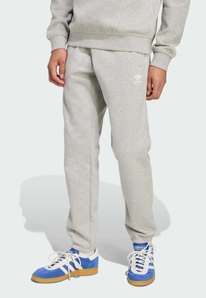 Grå sweatshirtbyxor med avslappnad passform, tillverkade av mjukt tyg, med sidfickor och en liten vit logotyp. I kombination med blå och vita sneakers.