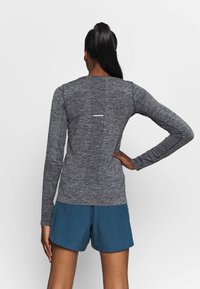 Long-sleeve black-and-gray heathered athletic top with a round neckline and a reflective strip on the back, paired with blue shorts.