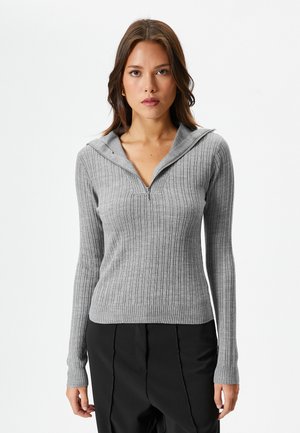 Grijs geribbeld langemouwer top met een ritssluiting op de mock neck en een aansluitende silhoutte. Zachte stof met een gestructureerd patroon. Gecombineerd met zwarte broek.