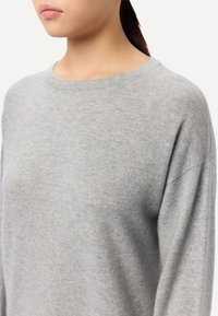 Pull gris en maille avec un col rond, des manches longues et une texture douce. Le tissu présente un motif chiné subtil et une coupe décontractée.