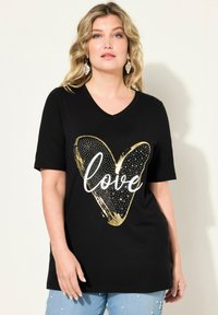 Svart t-shirt med v-ringning som har en guldig hjärt-design med texten "love". Materialet verkar mjukt; t-shirten har korta ärmar och en avslappnad passform.