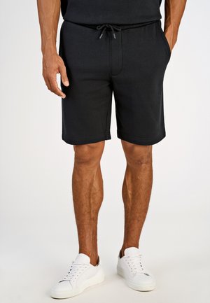 Shorts de sport noirs avec une taille élastique et un cordon de serrage, dotés de poches avant. Portés avec des baskets blanches. Texture lisse.