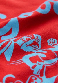 Sarkans audums ar zilām karikatūru grafiskām zīmēm. Dizainā ietverti rotaļīgi tēli ar dažādām izteiksmēm un stiliem, radot dzīvīgu rakstu.