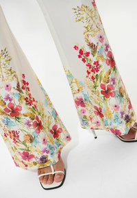 Pantaloni a palazzo floreali in tessuto leggero. Presentano fiori multicolori in rosso, blu e giallo su uno sfondo crema.
