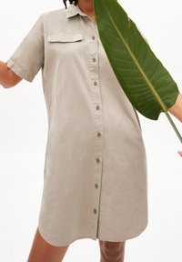 Robe chemise en lin beige clair avec un col, des manches courtes, une fermeture à boutons à l'avant et une poche plaquée. Texture lisse et coupe décontractée.