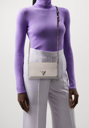 Světle šedá texturovaná kožená křížová taška s trojúhelníkovým logem, stříbrným řetízkovým popruhem a zavíráním na klopu, nošená přes fialový rolák.
