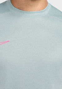 Vaaleansininen urheilupaita, jossa on sileä pinta, pyöreä pääntie ja etupuolella vaaleanpunainen logo.