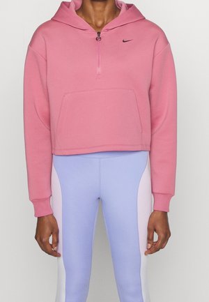 Osoba ubrana w różową, skróconą bluzę Nike z półzamkiem oraz legginsy w jasnoniebiesko-białe blokowe wzory.