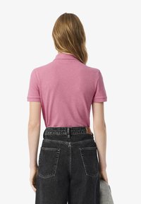 Polo shirt rosa con colletto, maniche corte, abbinato a jeans neri a vita alta con una patch in pelle e due tasche posteriori.