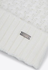 Witte gebreide muts met een gestructureerd patroon bovenop en een geribbelde sectie aan de onderkant. Voorzien van een zilveren logoplaatje met het opschrift "WITTCHEN."