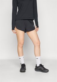 Musta pitkähihainen paita ja mustat urheilushortsit sivuhalkioilla. Valkea Nike-logo shortseissa. Mustat lenkkarit ja valkoiset sukat, joissa Nike-logo.