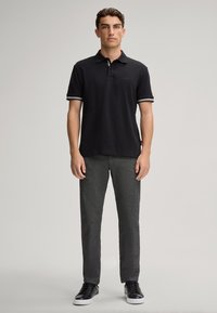 Zwart poloshirt met korte mouwen, witte gestreepte accenten op de kraag, gecombineerd met gestructureerde donkergrijze broeken en zwarte sneakers.