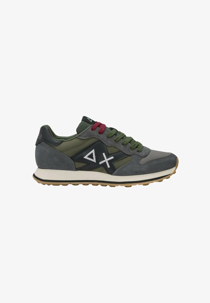 Chaussure de sport grise et verte avec des lacets rouges et verts, une semelle blanche, et un panneau latéral noir avec des symboles blancs en forme de triangle et de X.