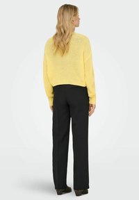 Dzeltena adīta fleece, īsa piegriezuma dizains, garas piedurknes, savienota ar melnajiem biksēm. Vienkārša un teksturēta bez ievērojamiem rakstiem vai akcents.