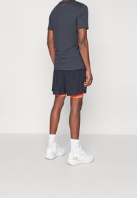 Camiseta atlética gris, pantalones cortos negros con acentos naranjas y zapatillas blancas con detalles amarillos. Diseño simple, tejido ligero.