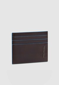 Tarjetero de cuero marrón con cuatro ranuras, costuras azules y un logo grabado en el lateral. Textura suave y diseño minimalista.