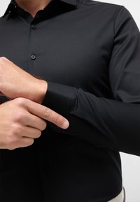 Maglietta a maniche lunghe nera con un design aderente. Presenta una chiusura con bottoni e dettagli sui polsini, realizzata in un tessuto morbido.