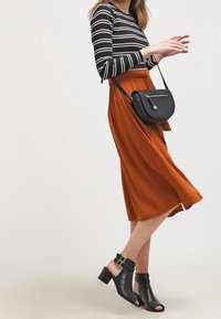 Stribet sort og hvid langærmet bluse med en orange midi-nederdel. Sorte sandaler med åbne tæer og spænde detalje samt en lille sort crossover-taske.
