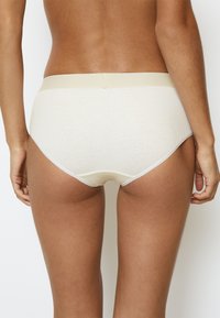 Slip in cotone beige con una texture a coste e un morbido elastico in vita. Presenta una cucitura a contrasto sottile attorno alle aperture delle gambe.
