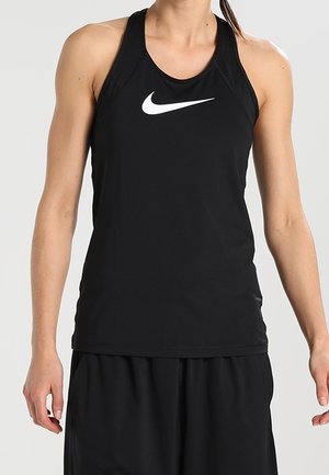 Sportowiec ubrany w czarny bezrękawnik Nike i czarne spodenki, stojący na tle jednolitego jasnego tła.