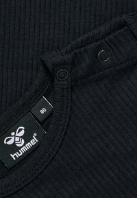 Svart ribbat tygplagg med rund hals, med två tryckknappar och en etikett med märket "hummel" och storlek 80.